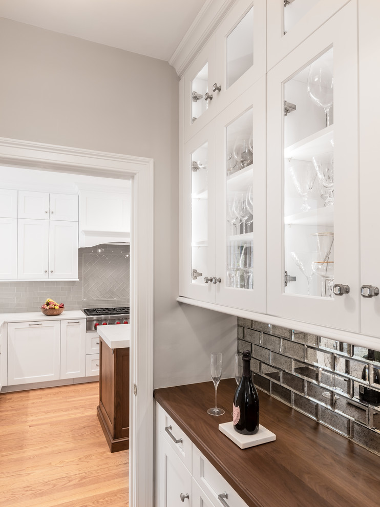 Klassisk inredning av ett kök, med en undermonterad diskho, vita skåp, bänkskiva i kvartsit, stänkskydd i glaskakel, rostfria vitvaror och en köksö
