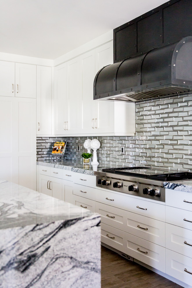 Idée de décoration pour une cuisine tradition en L avec un placard à porte shaker, des portes de placard blanches, une crédence métallisée, un électroménager en acier inoxydable, parquet foncé, îlot et un sol marron.