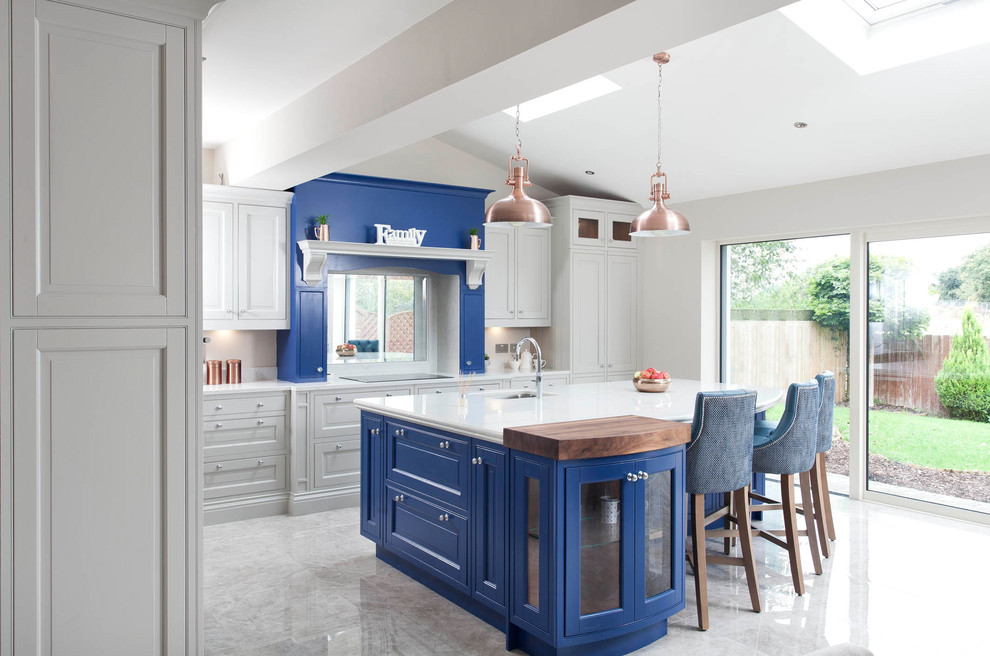This is an example of an expansive traditional l-shaped open plan kitchen in Dublin with an integrated sink, blue cabinets, quartz worktops, white splashback, stone slab splashback, stainless steel appliances, ceramic flooring, an island and beaded cabinets.
