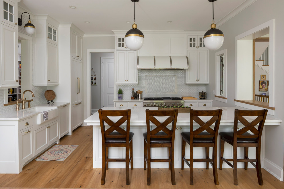 Kitchen - mid-sized transitional l-shaped medium tone wood floor and beige floor kitchen idea in Minneapolis with a farmhouse sink, shaker cabinets, white cabinets, white backsplash, ceramic backsplash, stainless steel appliances, a peninsula and white countertops