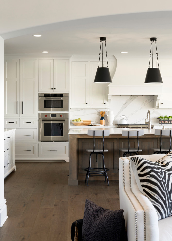 Design ideas for an expansive beach style l-shaped kitchen/diner in Minneapolis with a belfast sink, white cabinets, engineered stone countertops, white splashback, stainless steel appliances, medium hardwood flooring, an island, brown floors and white worktops.