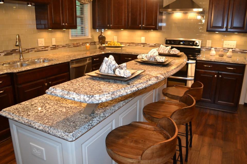 Klassisk inredning av ett mellanstort kök, med en nedsänkt diskho, luckor med upphöjd panel, skåp i mellenmörkt trä, granitbänkskiva, beige stänkskydd, stänkskydd i glaskakel, rostfria vitvaror, mellanmörkt trägolv och en köksö