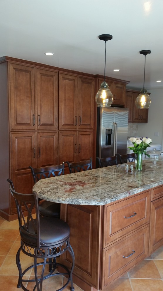 Eat-in kitchen - mid-sized traditional l-shaped terra-cotta tile eat-in kitchen idea in Santa Barbara with a farmhouse sink, raised-panel cabinets, medium tone wood cabinets, granite countertops, beige backsplash, stone tile backsplash, stainless steel appliances and an island