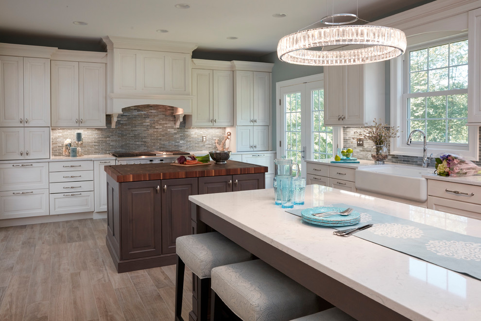 Expansive traditional u-shaped open plan kitchen in Baltimore with a belfast sink, raised-panel cabinets, white cabinets, engineered stone countertops, blue splashback, mosaic tiled splashback, stainless steel appliances, porcelain flooring, multiple islands, grey floors and white worktops.