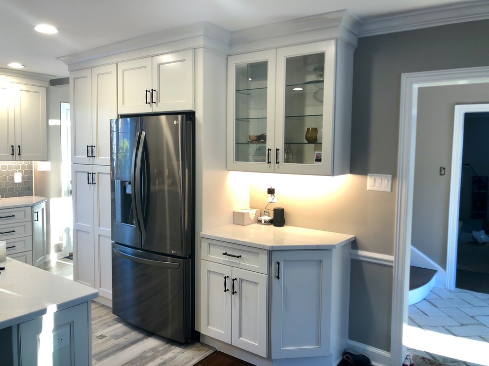 Inredning av ett klassiskt stort vit vitt kök, med en rustik diskho, luckor med infälld panel, beige skåp, bänkskiva i kvarts, grått stänkskydd, stänkskydd i porslinskakel, svarta vitvaror, vinylgolv, en halv köksö och flerfärgat golv