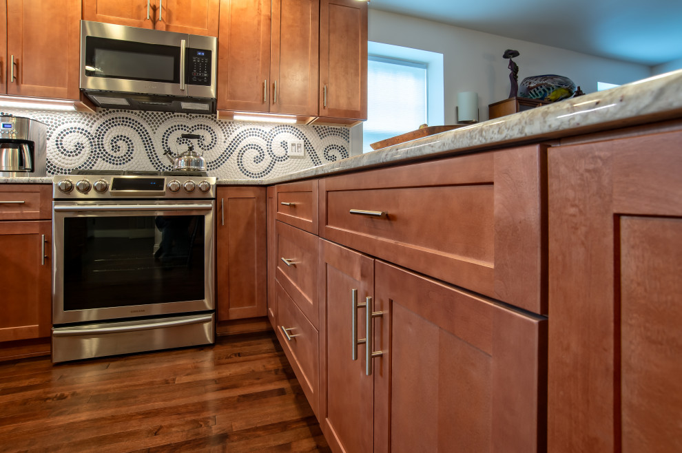Klassisk inredning av ett mellanstort grå grått kök, med en undermonterad diskho, skåp i shakerstil, skåp i ljust trä, granitbänkskiva, flerfärgad stänkskydd, stänkskydd i mosaik, rostfria vitvaror, målat trägolv, en halv köksö och brunt golv