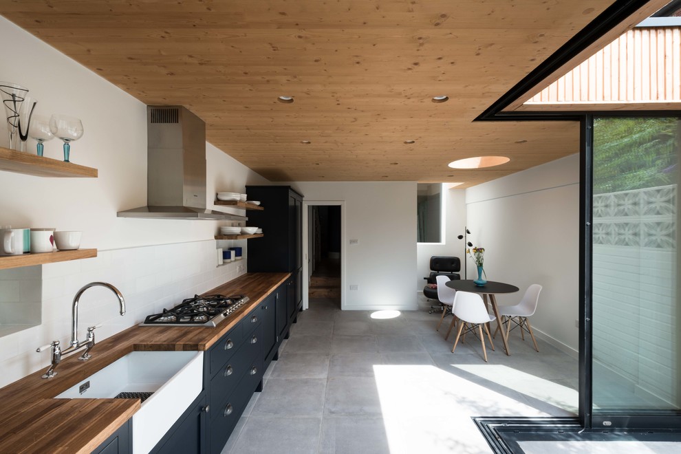 Einzeilige, Mittelgroße Moderne Wohnküche mit Landhausspüle, flächenbündigen Schrankfronten, schwarzen Schränken, Arbeitsplatte aus Holz, Küchenrückwand in Weiß und grauem Boden in London