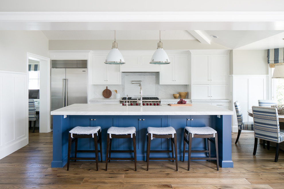 Zweizeilige Maritime Küche mit Schrankfronten im Shaker-Stil, weißen Schränken, Küchenrückwand in Weiß, Küchengeräten aus Edelstahl, braunem Holzboden und Kücheninsel in Los Angeles