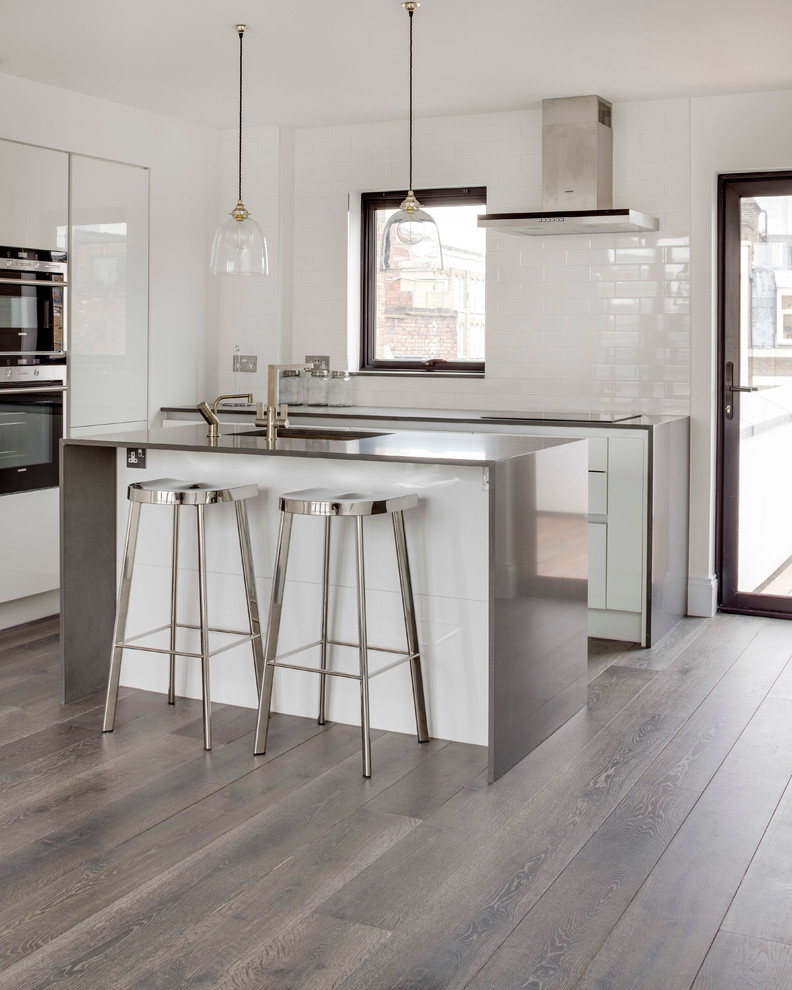 Moderne Küchenbar mit Unterbauwaschbecken, flächenbündigen Schrankfronten, weißen Schränken, Edelstahl-Arbeitsplatte, Küchenrückwand in Weiß, braunem Holzboden und Kücheninsel in London