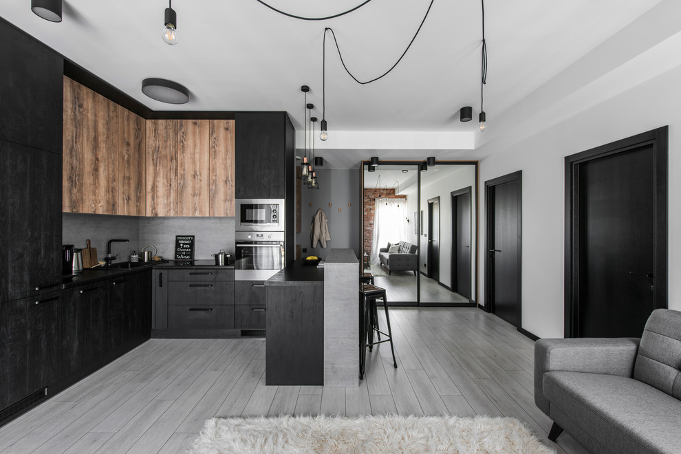 Cette photo montre une cuisine ouverte encastrable et grise et noire tendance en L de taille moyenne avec un placard à porte plane, des portes de placard noires, une crédence grise, une péninsule et un sol gris.
