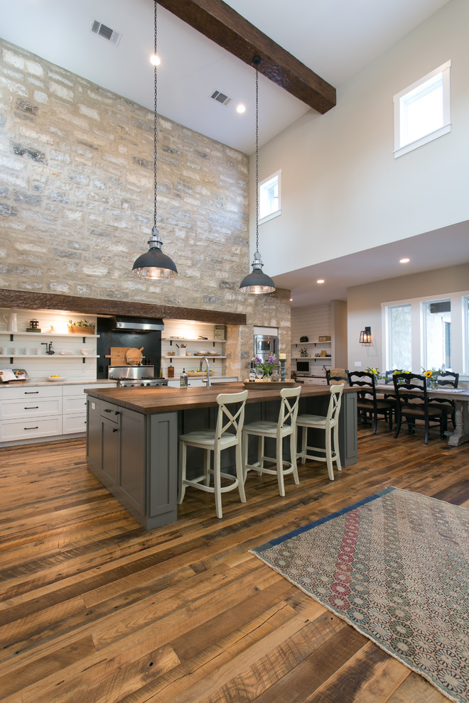 Example of a cottage medium tone wood floor kitchen design in Austin with a farmhouse sink, shaker cabinets, white cabinets, marble countertops, white backsplash, wood backsplash and stainless steel appliances