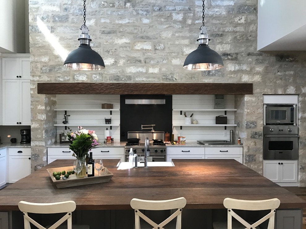 Inspiration for a large rural l-shaped open plan kitchen in Austin with a belfast sink, shaker cabinets, white cabinets, wood worktops, white splashback, wood splashback, stainless steel appliances, dark hardwood flooring, an island and brown floors.