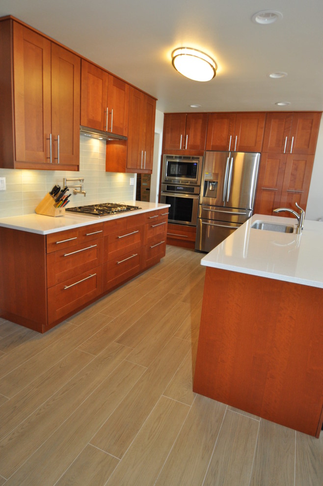 Example of a mid-sized trendy u-shaped ceramic tile eat-in kitchen design in Los Angeles with an undermount sink, shaker cabinets, brown cabinets, quartzite countertops, blue backsplash, glass tile backsplash, stainless steel appliances and an island