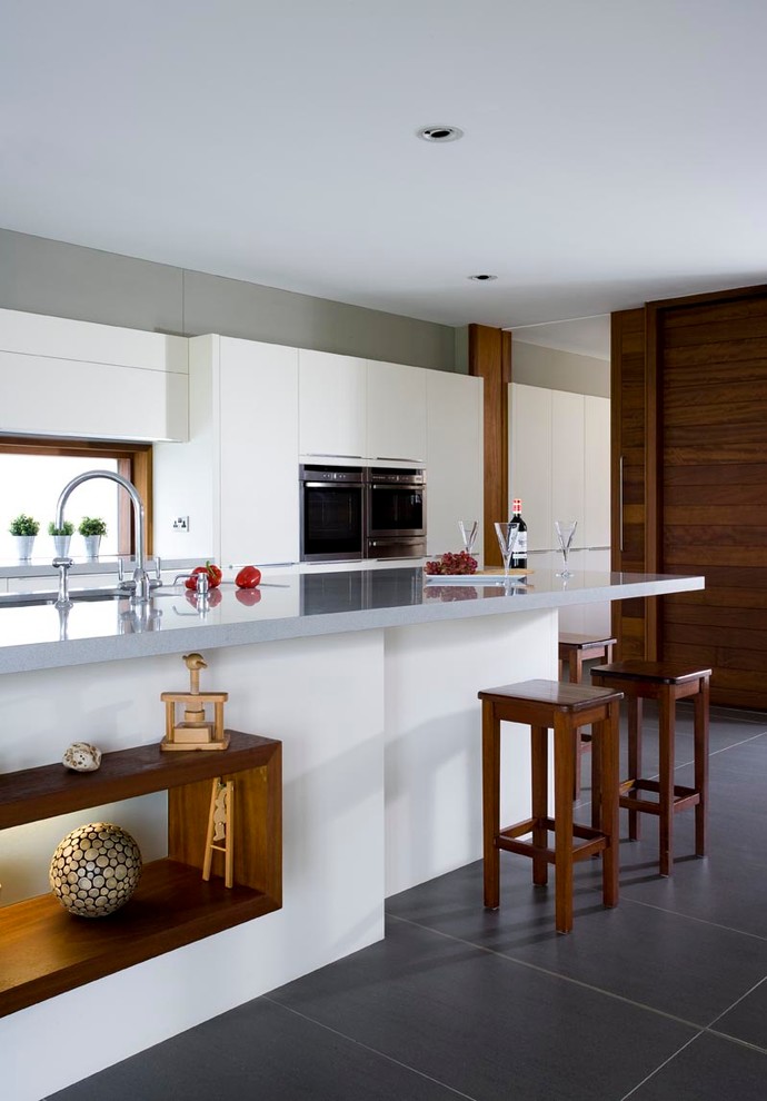 Exempel på ett stort modernt linjärt kök med öppen planlösning, med en enkel diskho, släta luckor, vita skåp, granitbänkskiva, vitt stänkskydd, glaspanel som stänkskydd, rostfria vitvaror, klinkergolv i keramik och en köksö