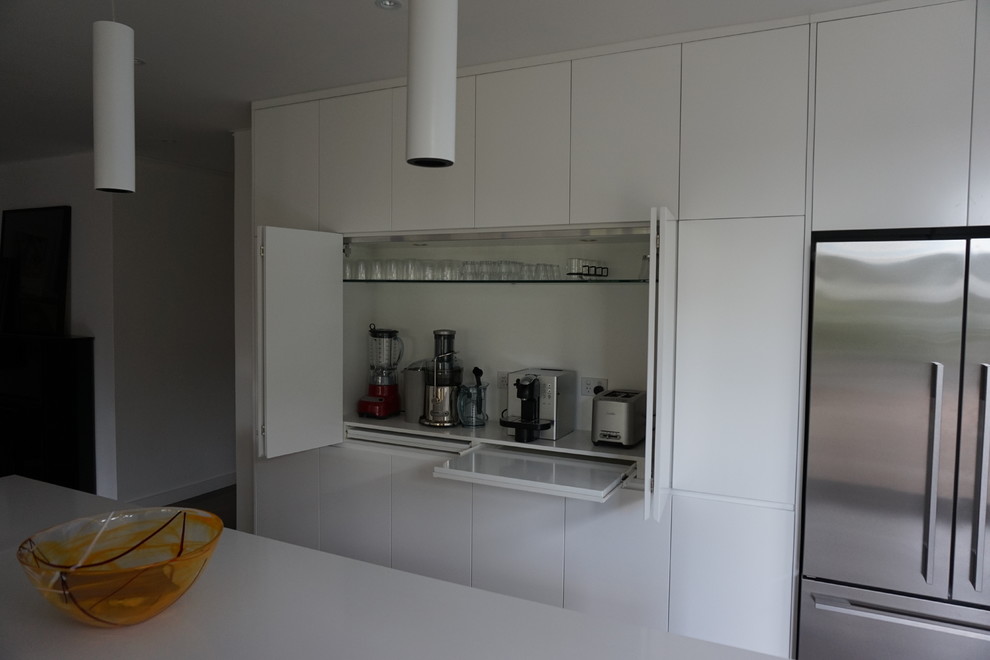 Bild på ett mellanstort funkis kök, med en undermonterad diskho, släta luckor, vita skåp, bänkskiva i kvarts, vitt stänkskydd, rostfria vitvaror, klinkergolv i keramik, en köksö och glaspanel som stänkskydd