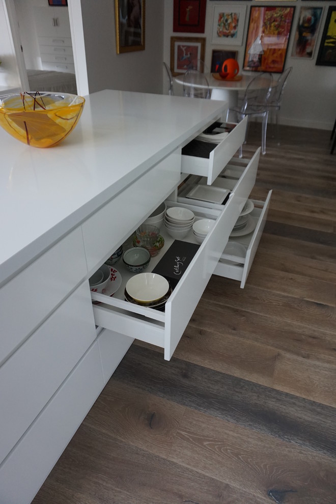 Modern inredning av ett mellanstort kök, med en undermonterad diskho, släta luckor, vita skåp, bänkskiva i kvarts, vitt stänkskydd, rostfria vitvaror, klinkergolv i keramik, en köksö och glaspanel som stänkskydd