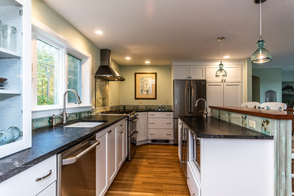 Example of a mid-sized classic l-shaped medium tone wood floor and brown floor open concept kitchen design with an undermount sink, shaker cabinets, white cabinets, granite countertops, green backsplash, stainless steel appliances and an island
