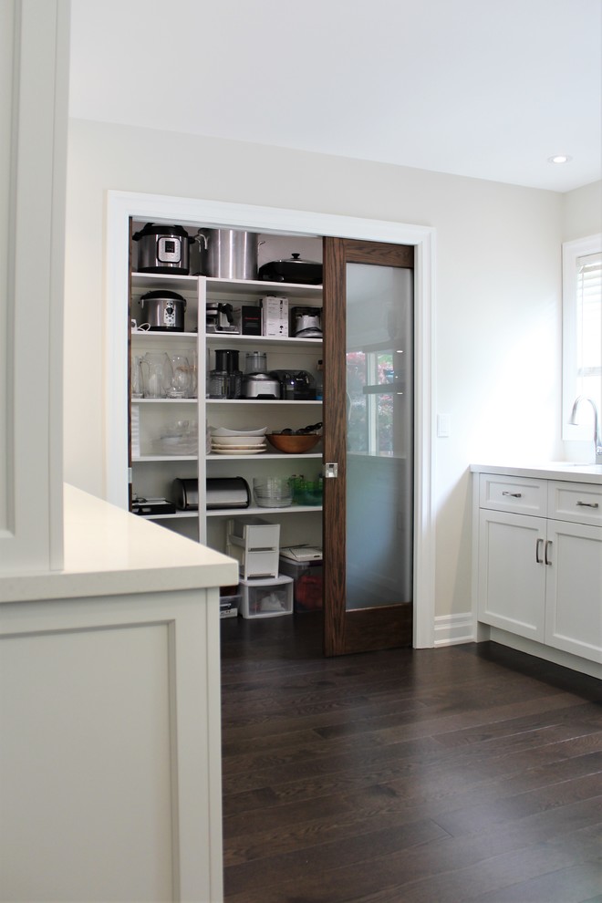 This is an example of a large classic kitchen pantry in Toronto with a double-bowl sink, white cabinets, engineered stone countertops, white splashback, marble splashback, stainless steel appliances, dark hardwood flooring, an island, brown floors and white worktops.