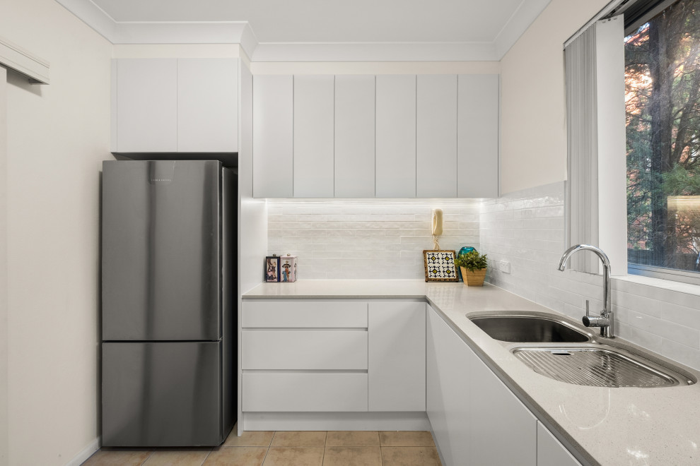 Design ideas for a medium sized modern u-shaped enclosed kitchen in Sydney with a submerged sink, flat-panel cabinets, white cabinets, engineered stone countertops, white splashback, metro tiled splashback, stainless steel appliances, ceramic flooring, brown floors and beige worktops.