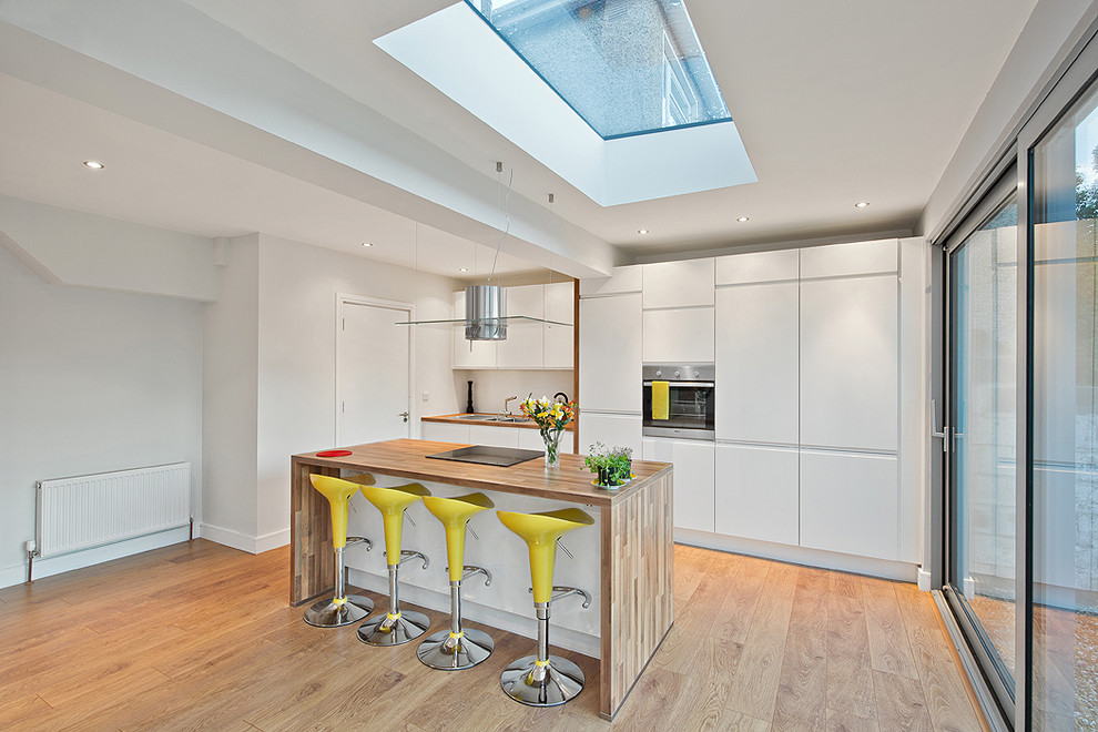 Mittelgroße, Zweizeilige Moderne Küche mit flächenbündigen Schrankfronten, weißen Schränken, Küchengeräten aus Edelstahl, braunem Holzboden und Kücheninsel in Dublin