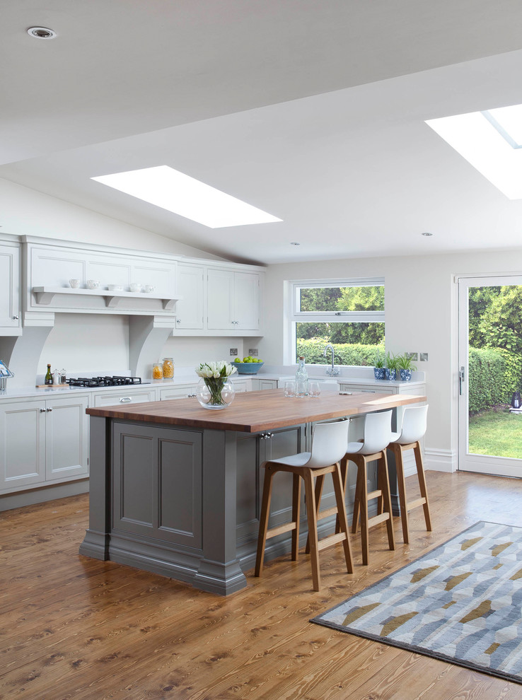 Inspiration for a large traditional l-shaped open plan kitchen in Dublin with a belfast sink, beaded cabinets, grey cabinets, quartz worktops, grey splashback, stone slab splashback, stainless steel appliances, medium hardwood flooring, an island and brown floors.