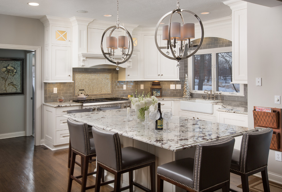 Example of a large classic u-shaped medium tone wood floor kitchen design in Columbus with a farmhouse sink, beaded inset cabinets, white cabinets, granite countertops, gray backsplash, glass tile backsplash, stainless steel appliances and an island