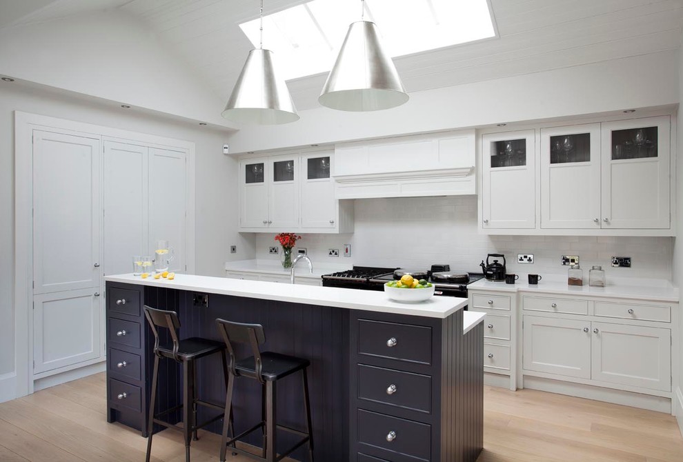 Foto de cocina de estilo de casa de campo con armarios estilo shaker, puertas de armario blancas, salpicadero blanco, suelo de madera clara y una isla