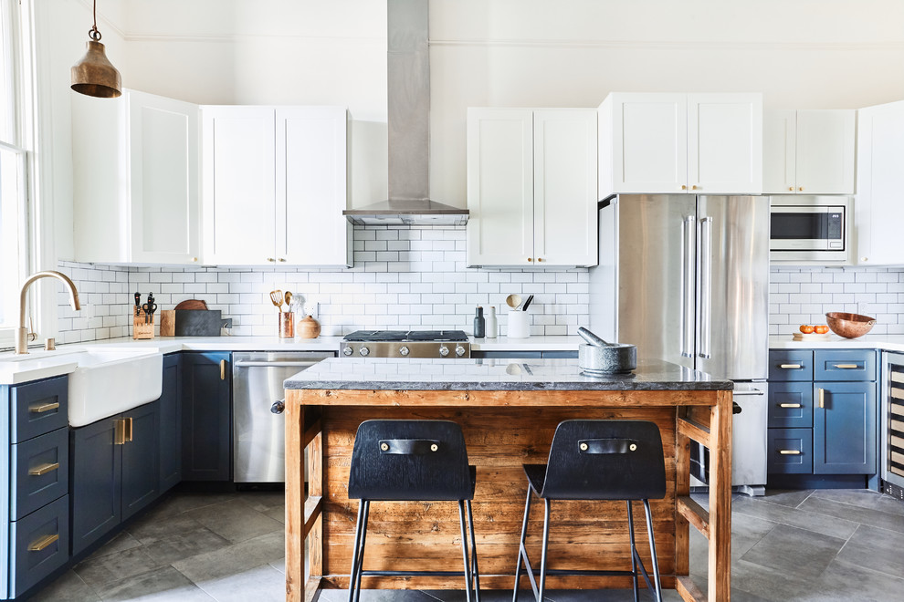 Inspiration for a medium sized traditional l-shaped kitchen/diner in San Francisco with a belfast sink, shaker cabinets, white cabinets, engineered stone countertops, white splashback, ceramic splashback, stainless steel appliances, slate flooring, an island, grey floors and white worktops.