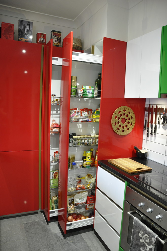 Modern inredning av ett kök, med en dubbel diskho, röda skåp, vitt stänkskydd, stänkskydd i tunnelbanekakel, rostfria vitvaror och klinkergolv i keramik
