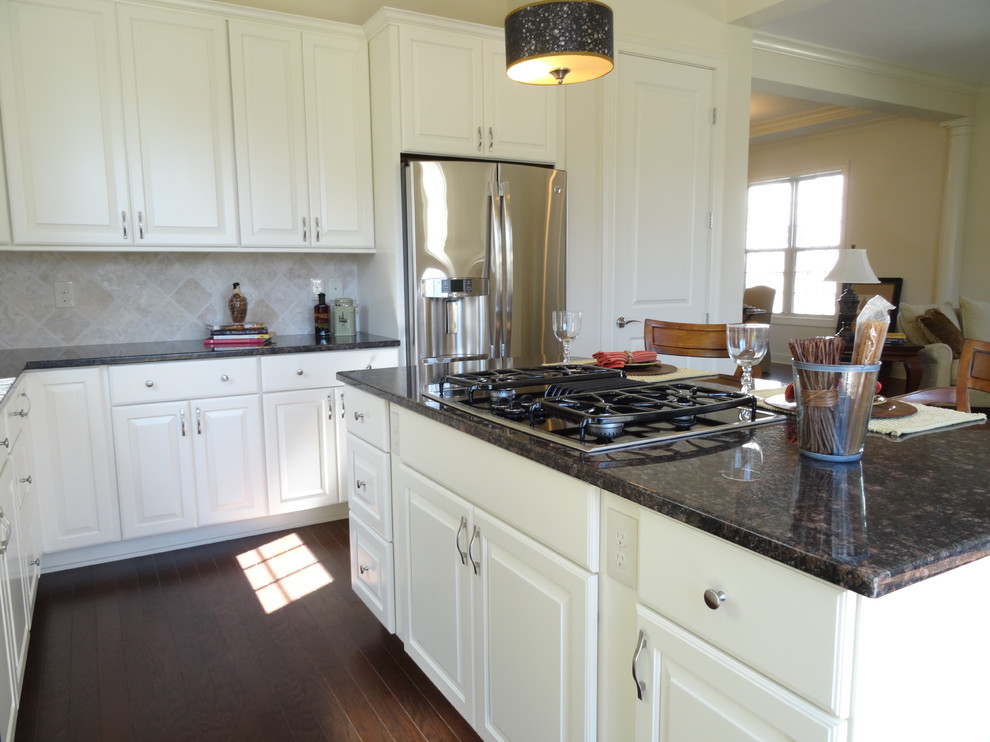 Inspiration for a medium sized classic l-shaped enclosed kitchen in Columbus with granite worktops, a submerged sink, raised-panel cabinets, white cabinets, beige splashback, travertine splashback, stainless steel appliances, dark hardwood flooring, an island and brown floors.