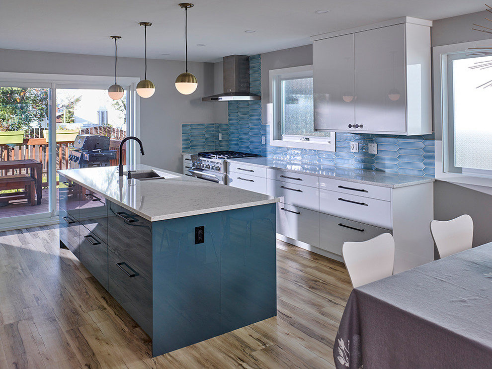 Example of a 1960s beige floor kitchen design in Edmonton with an undermount sink, flat-panel cabinets, blue backsplash, stainless steel appliances and an island