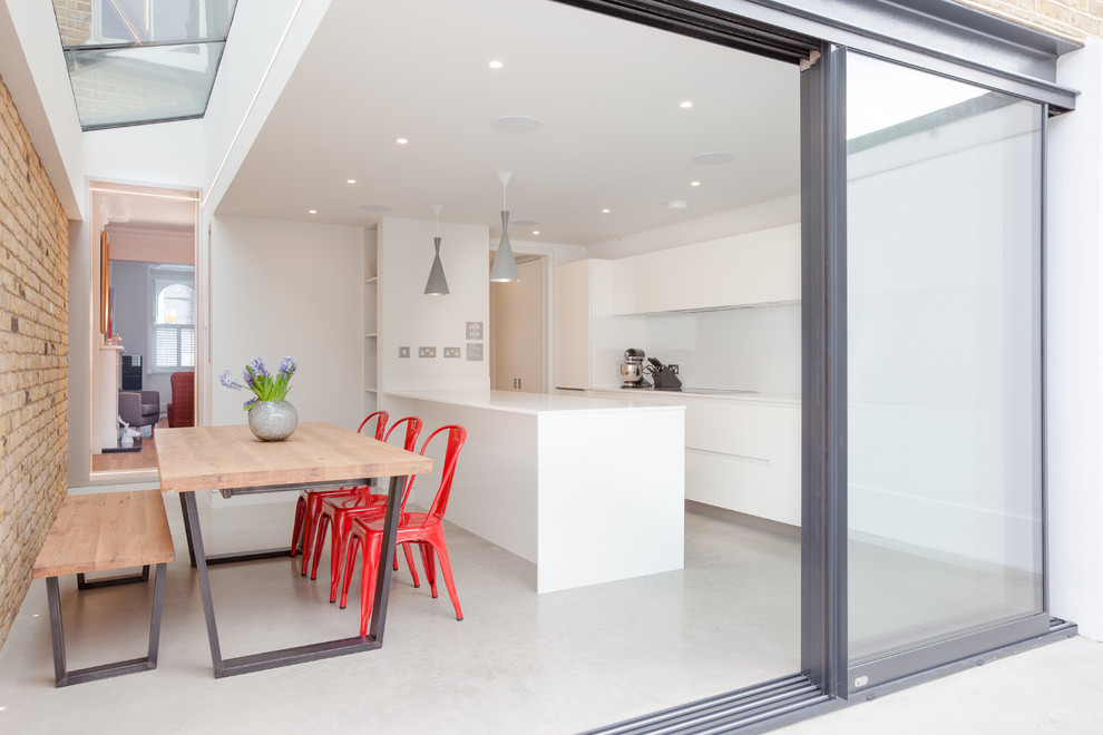Идея дизайна: прямая кухня в современном стиле с обеденным столом, плоскими фасадами, белыми фасадами, белым фартуком, фартуком из стекла, бетонным полом и полуостровом