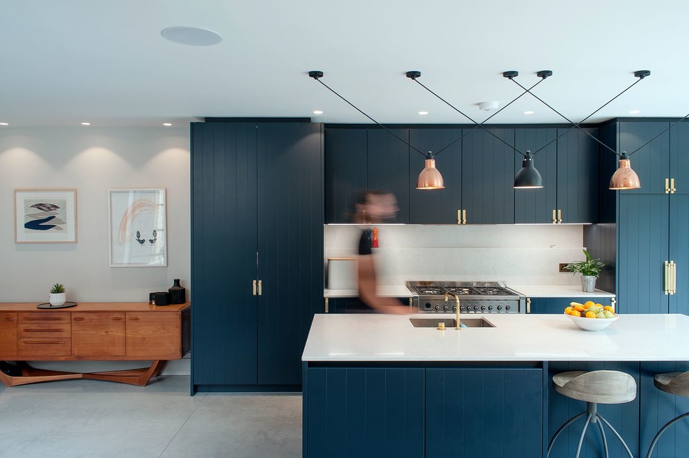 Medium sized classic galley kitchen/diner in London with a double-bowl sink, beaded cabinets, blue cabinets, white splashback, stainless steel appliances, concrete flooring, an island and grey floors.