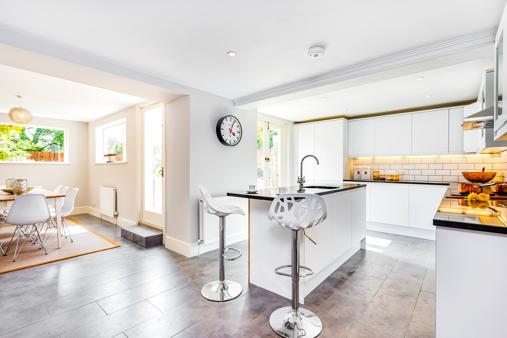 Moderne Küche in L-Form mit Unterbauwaschbecken, flächenbündigen Schrankfronten, Küchenrückwand in Weiß, Rückwand aus Metrofliesen, Küchengeräten aus Edelstahl und Kücheninsel in London