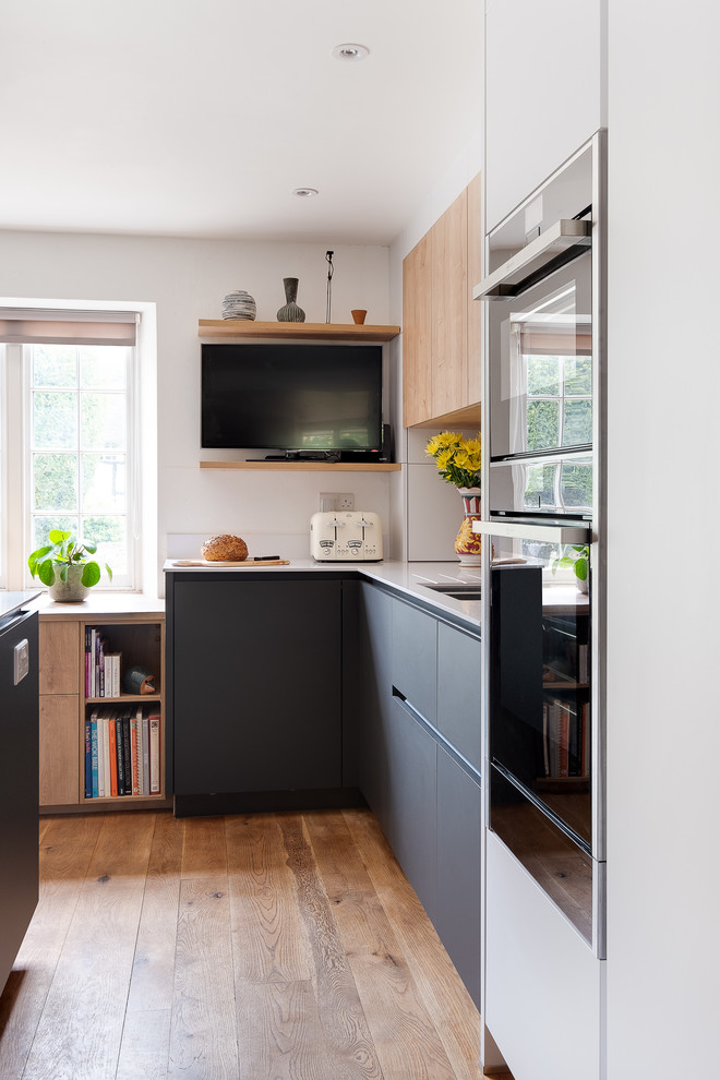 Esempio di una cucina moderna di medie dimensioni con lavello da incasso, ante lisce, top in superficie solida, paraspruzzi in legno, elettrodomestici neri, pavimento beige e top bianco