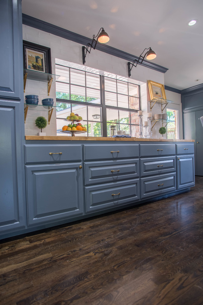Exempel på ett stort klassiskt kök, med en rustik diskho, luckor med upphöjd panel, blå skåp, träbänkskiva, vitt stänkskydd, stänkskydd i keramik, rostfria vitvaror, mörkt trägolv, en köksö och svart golv