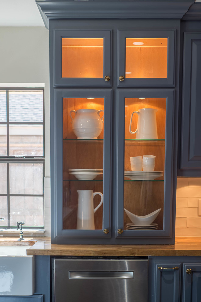 Klassisk inredning av ett stort kök, med en rustik diskho, luckor med upphöjd panel, blå skåp, träbänkskiva, vitt stänkskydd, stänkskydd i keramik, rostfria vitvaror, mörkt trägolv, en köksö och svart golv