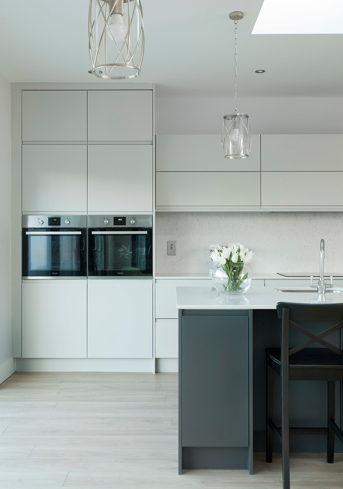 Expansive contemporary single-wall open plan kitchen in Other with an integrated sink, flat-panel cabinets, grey cabinets, quartz worktops, white splashback, stone slab splashback, stainless steel appliances, medium hardwood flooring, an island, brown floors and white worktops.