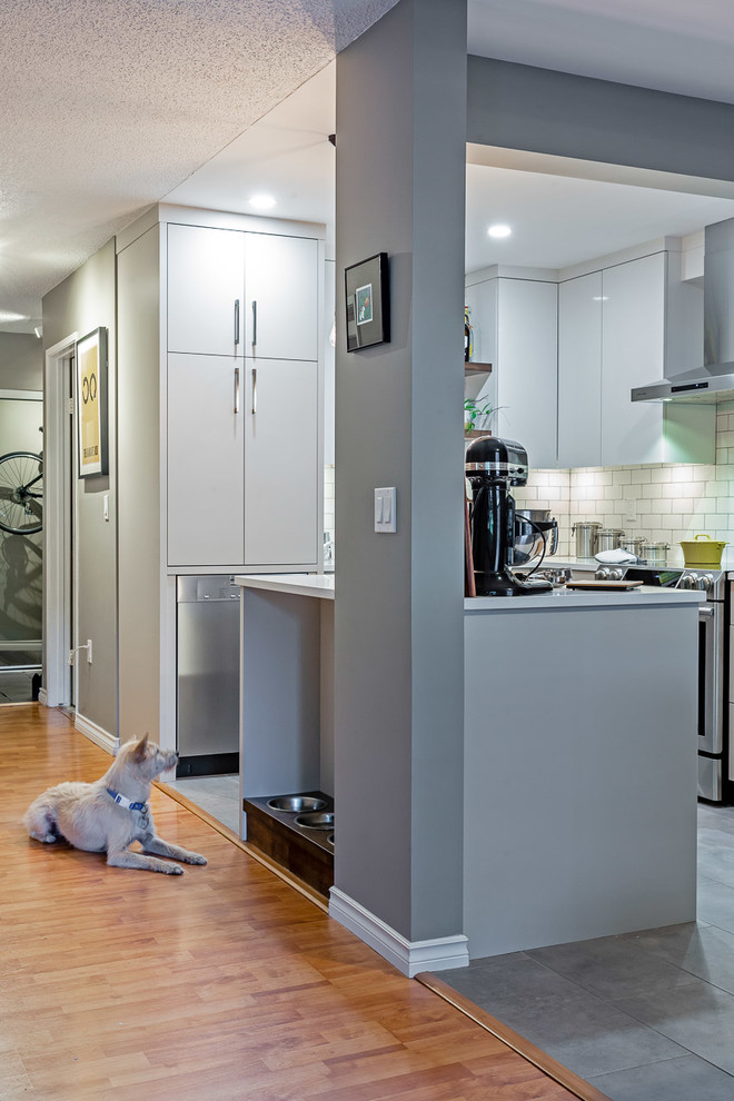 Modern inredning av ett litet vit vitt l-kök, med en undermonterad diskho, släta luckor, grå skåp, bänkskiva i kvarts, vitt stänkskydd, stänkskydd i tunnelbanekakel, rostfria vitvaror, cementgolv, en köksö och grått golv