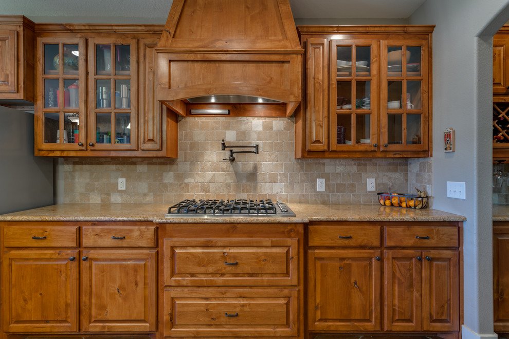 Rustik inredning av ett mellanstort kök, med en rustik diskho, luckor med upphöjd panel, skåp i mellenmörkt trä, granitbänkskiva, beige stänkskydd, stänkskydd i travertin, rostfria vitvaror, betonggolv, en köksö och brunt golv