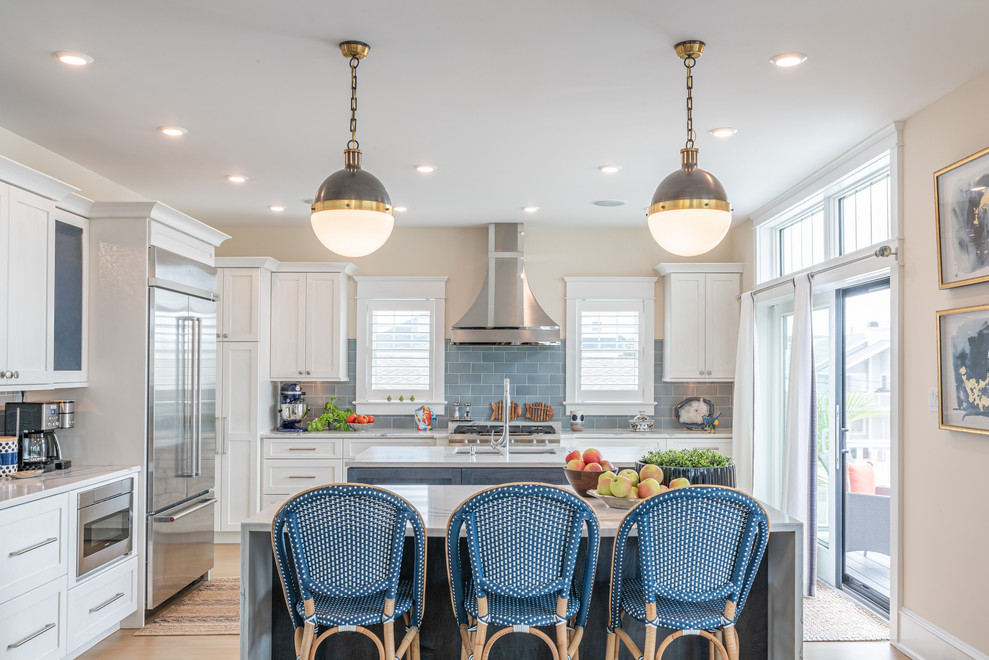 This is an example of a classic l-shaped kitchen in Philadelphia with a submerged sink, shaker cabinets, white cabinets, blue splashback, stainless steel appliances, light hardwood flooring, multiple islands, beige floors and grey worktops.