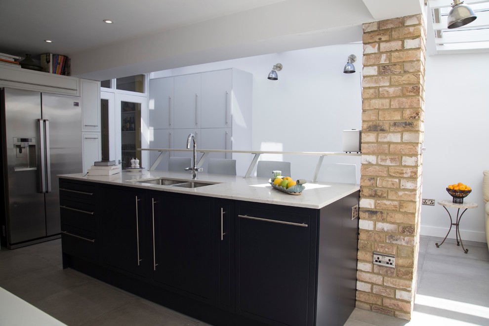 This is an example of a medium sized contemporary single-wall kitchen/diner in London with a double-bowl sink, flat-panel cabinets, quartz worktops, white splashback, metro tiled splashback, stainless steel appliances, porcelain flooring, an island, grey floors and white worktops.