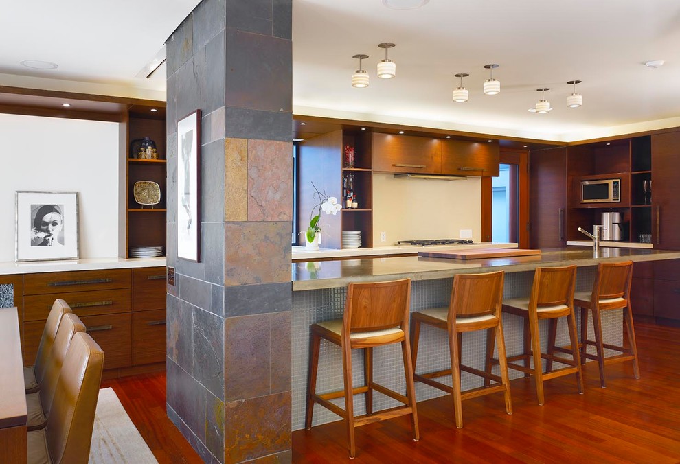 Cette photo montre une cuisine américaine encastrable tendance en L et bois brun de taille moyenne avec un placard à porte plane, un plan de travail en béton, une crédence blanche, un sol en bois brun et îlot.