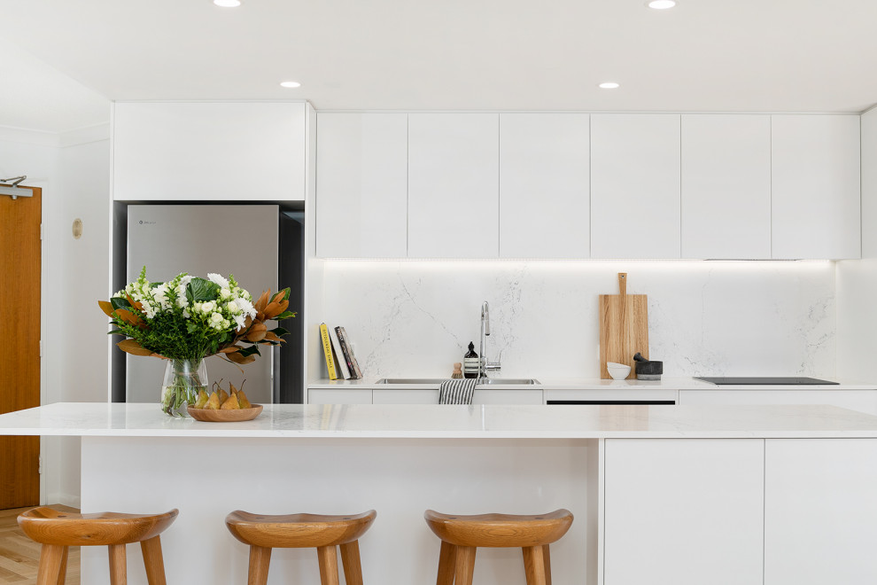 Foto de cocina contemporánea pequeña abierta con fregadero bajoencimera, salpicadero blanco, electrodomésticos negros, suelo de madera clara, una isla y encimeras blancas