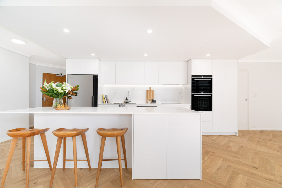 Immagine di una piccola cucina minimal con lavello sottopiano, paraspruzzi bianco, elettrodomestici neri, parquet chiaro e top bianco