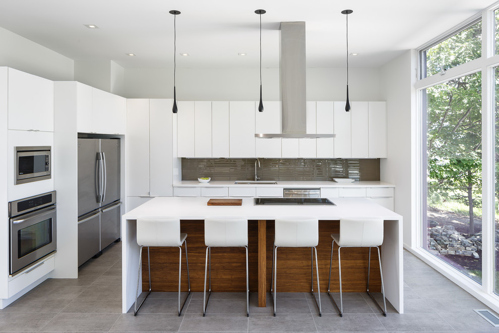 Minimalist galley concrete floor open concept kitchen photo in Ottawa with flat-panel cabinets, white cabinets, brown backsplash, glass tile backsplash, stainless steel appliances and an island