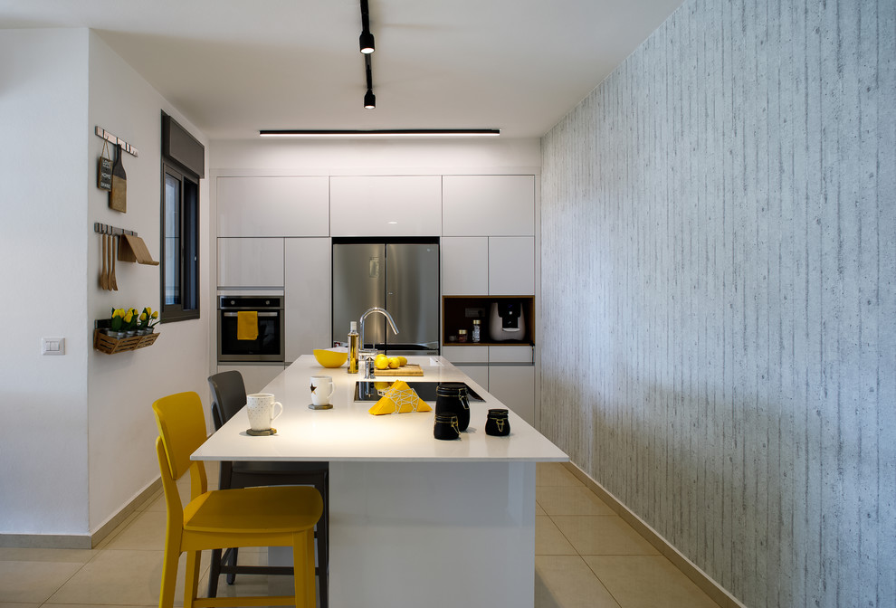 На фото: кухня в современном стиле с плоскими фасадами, белыми фасадами, техникой из нержавеющей стали, островом и бежевым полом с