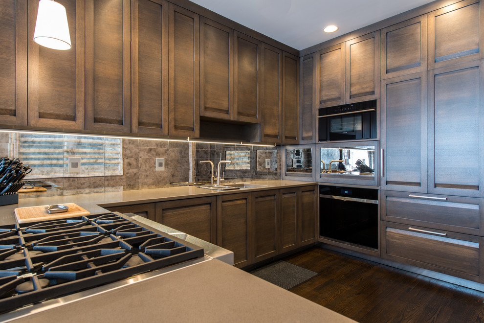 Medium sized contemporary u-shaped open plan kitchen in Chicago with an integrated sink, recessed-panel cabinets, grey cabinets, engineered stone countertops, metallic splashback, mirror splashback, integrated appliances, dark hardwood flooring, a breakfast bar and brown floors.
