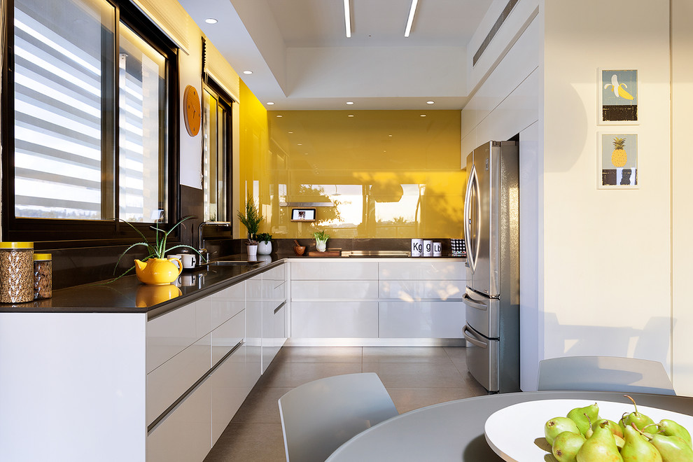 Exemple d'une cuisine moderne fermée et de taille moyenne avec un placard à porte plane, des portes de placard blanches, un plan de travail en surface solide, une crédence jaune, une crédence en feuille de verre et aucun îlot.