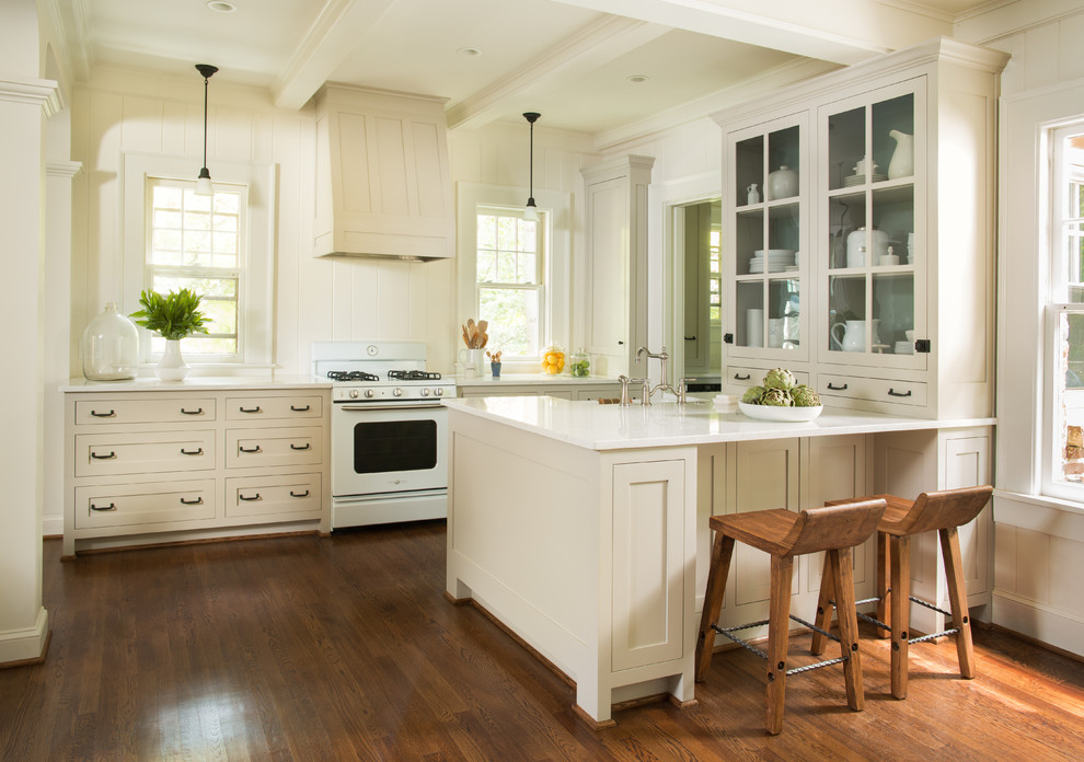 Klassische Küche mit beigen Schränken, Quarzwerkstein-Arbeitsplatte, Küchenrückwand in Weiß, weißen Elektrogeräten, braunem Holzboden, Halbinsel und Glasfronten in Atlanta
